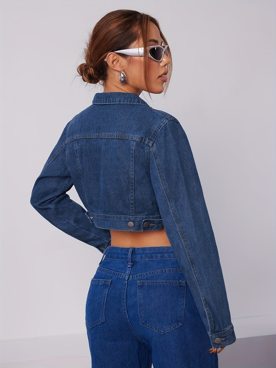 Frau in blauer Jeansjacke und Jeans, trägt Sonnenbrille, modisches Outfit, Rückansicht.