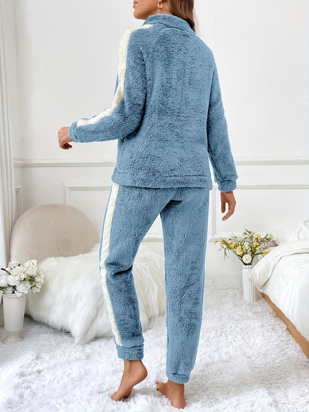 Frau in blauem Fleece-Pyjama-Set mit Streifen, gemütlich, Schlafzimmer, Blumen, Teppich.