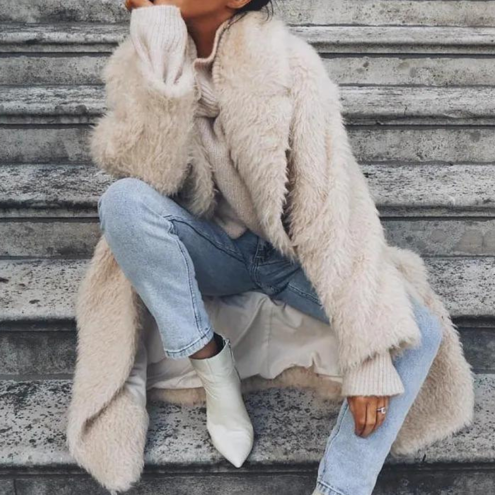 Frau in beigem Kunstpelzmantel, blauer Jeans und weißen Stiefeletten auf Treppe sitzend.