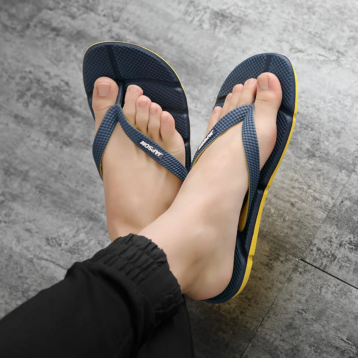 Blaue Flip-Flops mit gelber Sohle auf grauem Boden, getragen von einer Person.