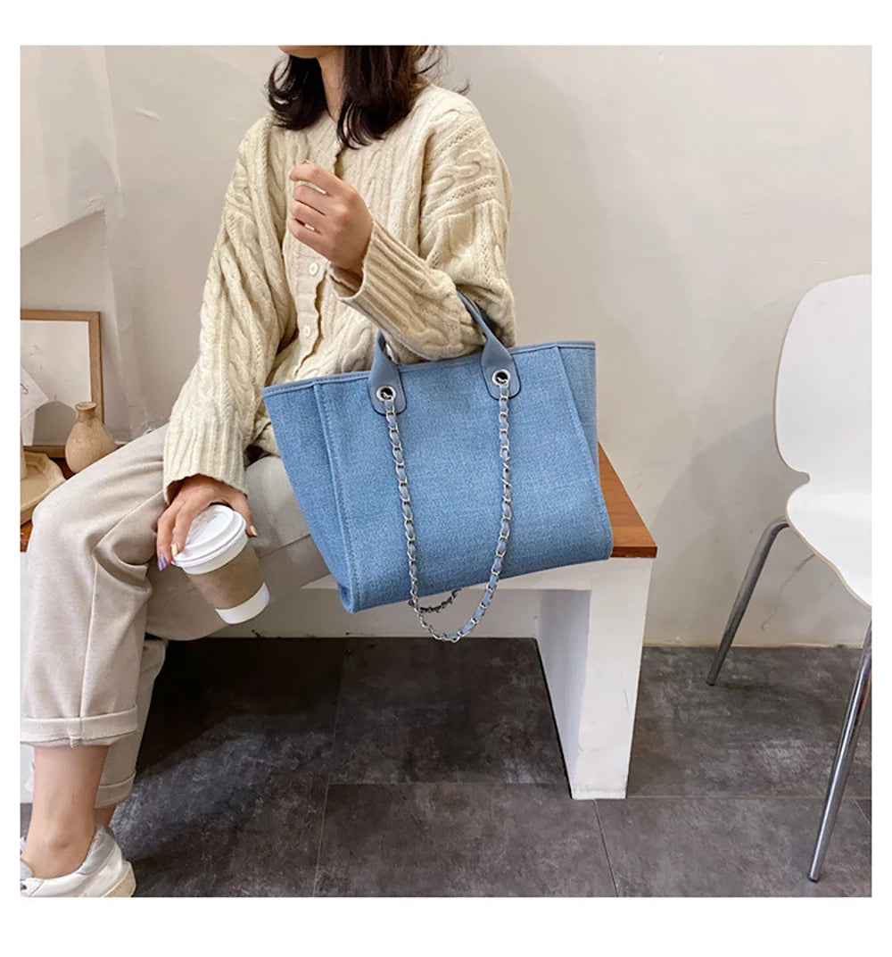 Frau mit hellblauer Jeanshandtasche, Kettengriff, beige Strickjacke, Kaffeetasse.