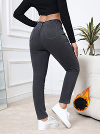 Frau in grauer Jeans, schwarzes Oberteil, weiße Sneaker, Wohnzimmer, Pflanze, Sofa, Feuer.