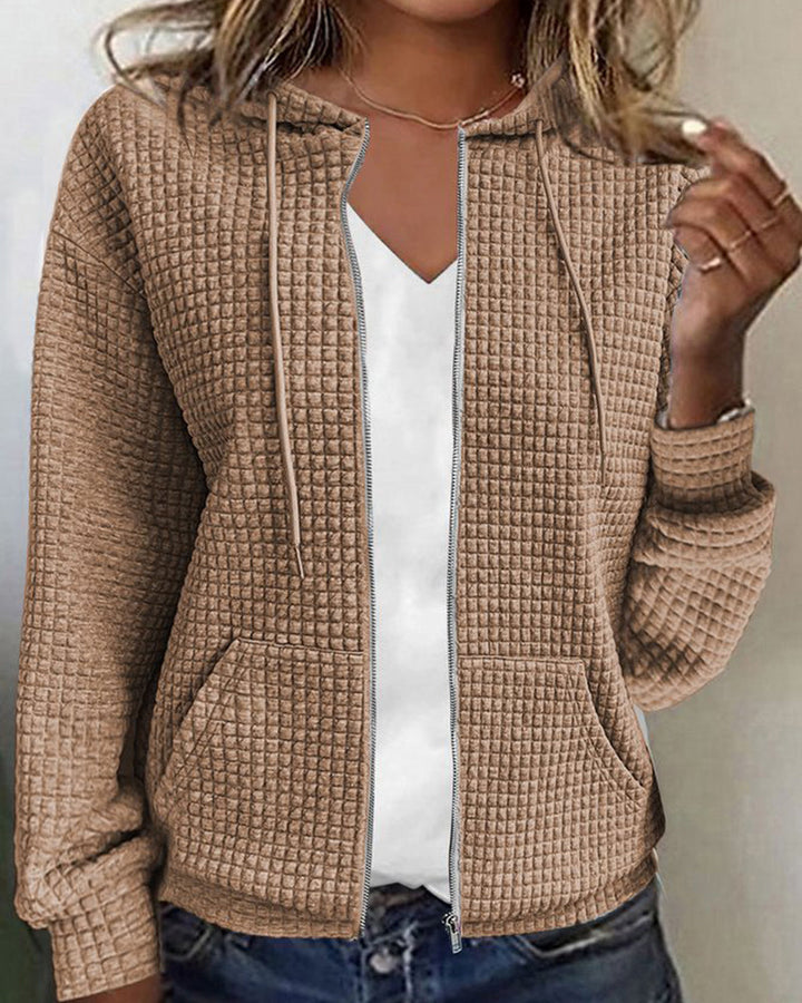Frau trägt beige Kapuzenjacke mit Waffelmuster, Reißverschluss, lässig, modisch, Herbstmode.
