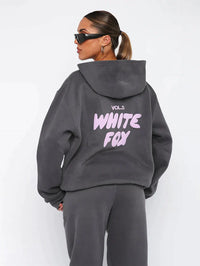 Frau in grauem Hoodie mit "White Fox" Aufdruck, Sonnenbrille, lässiger Stil.