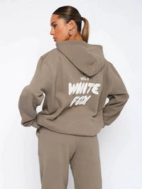 Frau in braunem Hoodie mit "White Fox" Aufdruck, Kapuze, lässiger Stil, Streetwear-Mode.