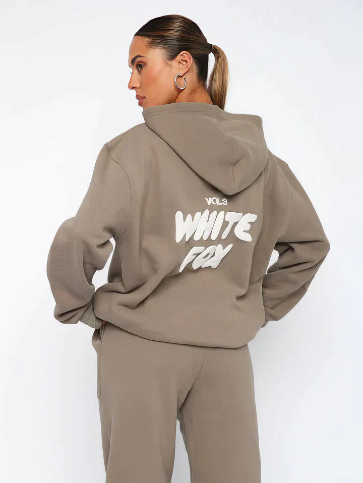 Frau in braunem Hoodie mit "White Fox" Aufdruck, Kapuze, lässiger Stil, Streetwear-Mode.