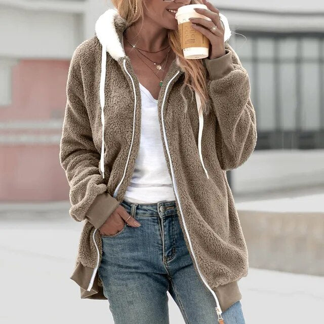 Frau in khakifarbener Fleecejacke mit Kapuze, hält Kaffeebecher, lässiger Herbstlook.