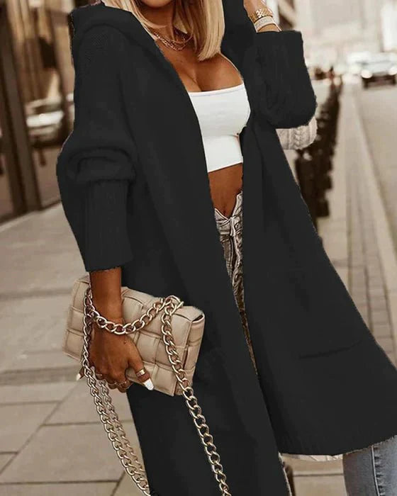 Frau in schwarzem Cardigan mit Kapuze, weißem Top, Jeans, beige Tasche, Straße im Hintergrund.