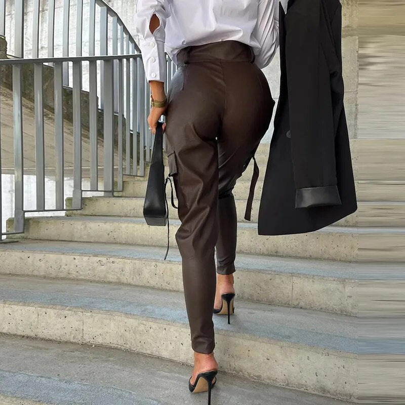 Frau in brauner Lederhose und weißer Bluse auf Treppe, modisch, elegant, High Heels.