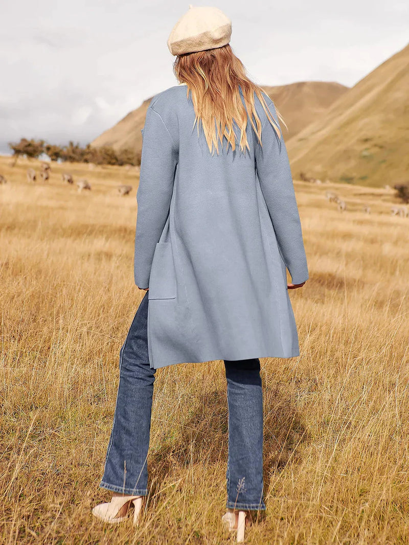 Frau in hellblauem Mantel und Jeans auf Wiese, beige Mütze, Herbstmode, Naturhintergrund.