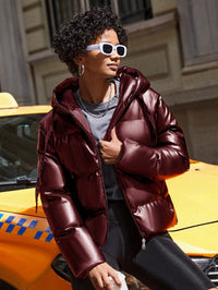 Frau in glänzender, burgunderroter Daunenjacke vor gelbem Taxi, modisch, urban.