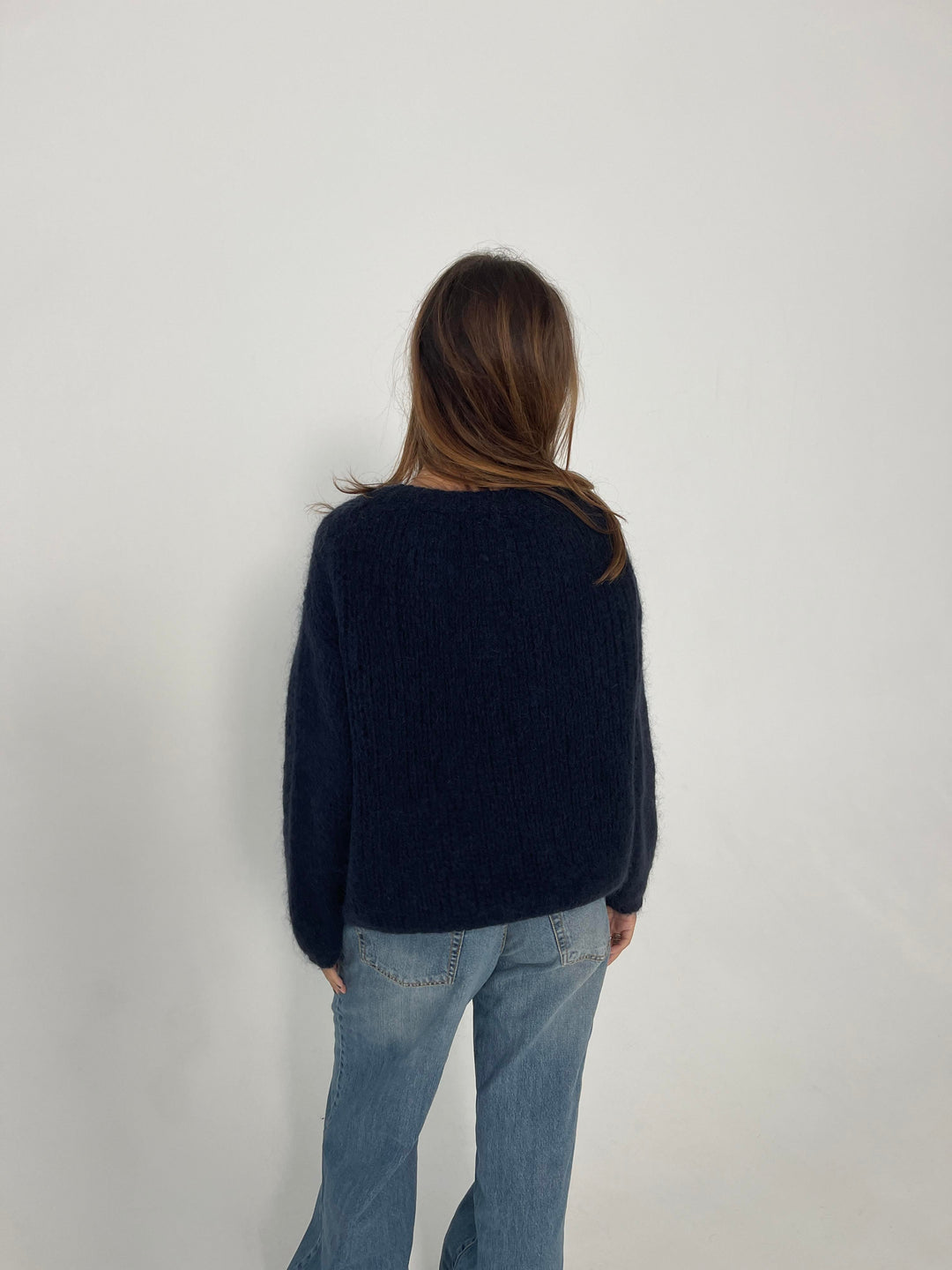 Frau in dunkelblauem Pullover und blauer Jeans, Rückansicht, minimalistisch, Modefotografie.