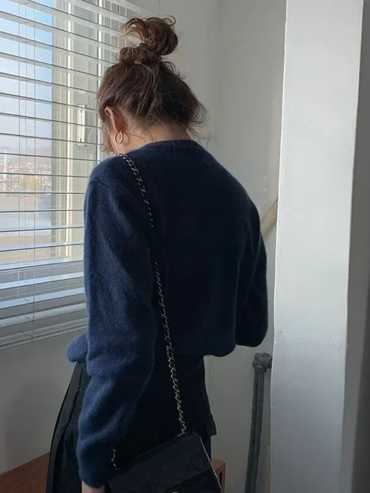 Frau in dunkelblauem Pullover mit schwarzer Tasche, steht vor Fenster, lässiger Look.