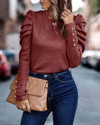 Frau in rotem Rüschenpullover, blaue Jeans, beige Clutch, Straße im Hintergrund.