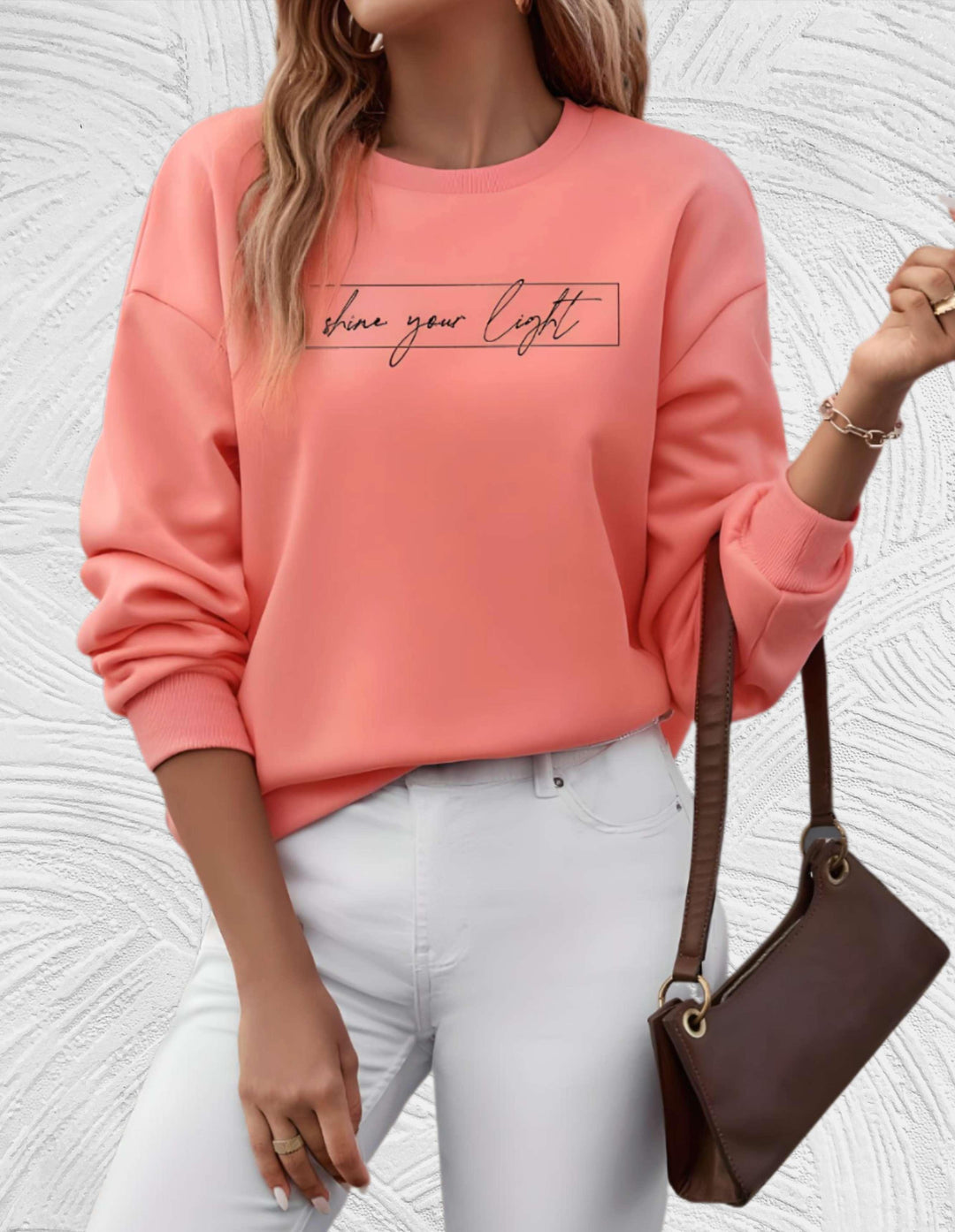Frau in rosa Sweatshirt mit Schriftzug, weiße Hose, braune Tasche, modisch, lässiger Stil.