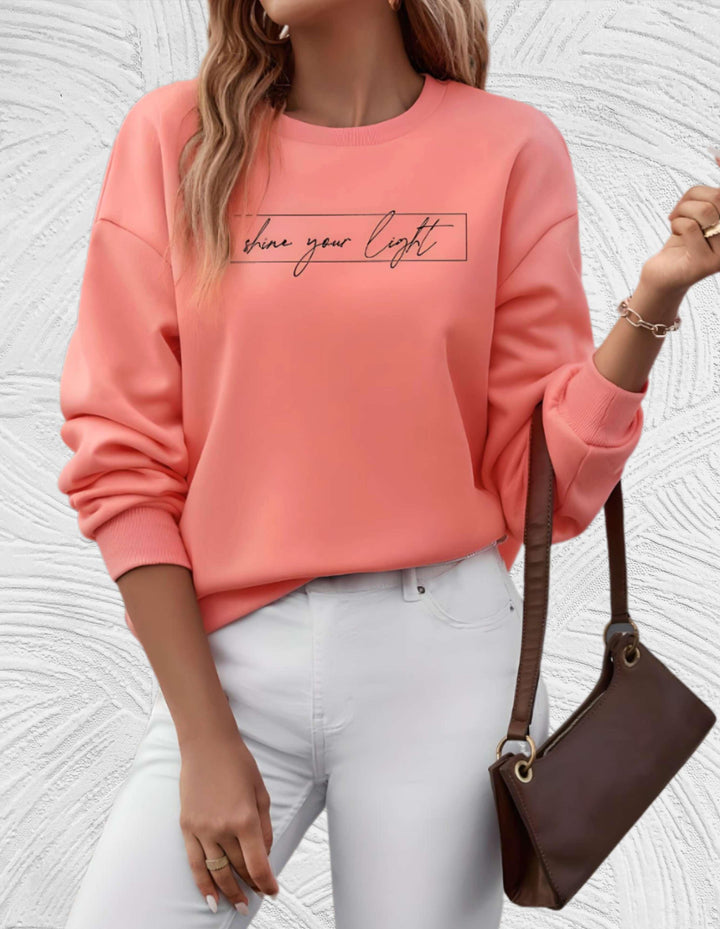 Frau in rosa Sweatshirt mit Schriftzug, weiße Hose, braune Tasche, modisch, lässiger Stil.