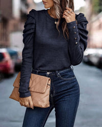 Frau in dunkelblauem Pullover mit Rüschenärmeln, hält beige Clutch, trägt Jeans.
