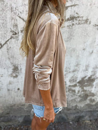 Frau in beigem Samt-Blazer und Jeansshorts vor Betonwand, lässige Mode.