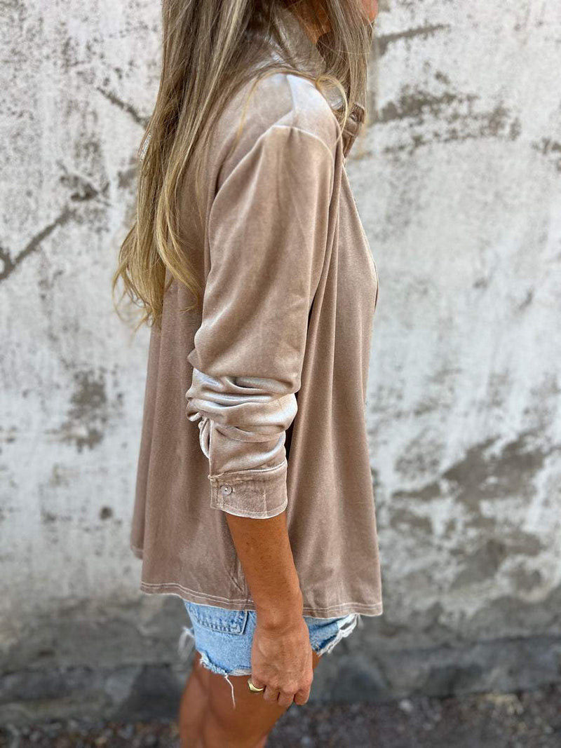 Frau in beigem Samt-Blazer und Jeansshorts vor Betonwand, lässige Mode.