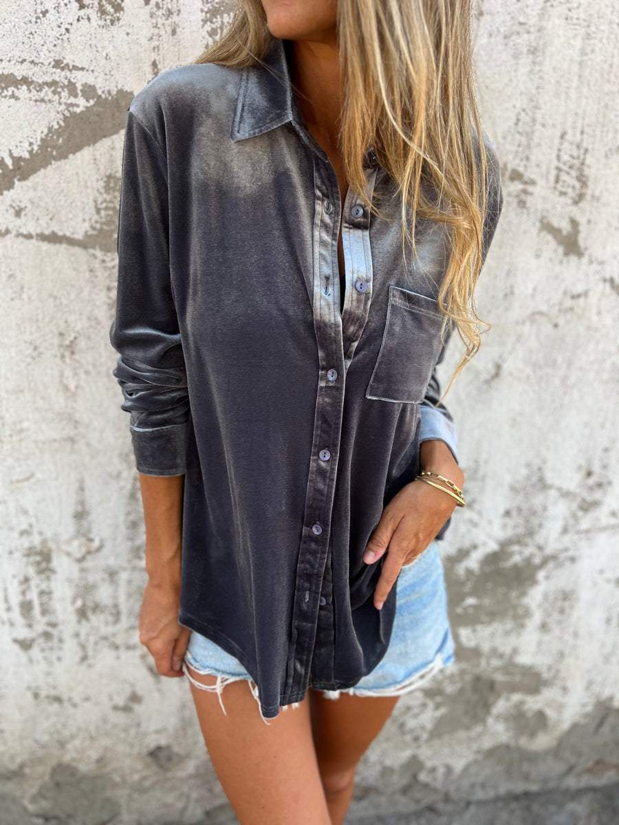 Frau in grauem Samthemd und Jeansshorts vor Betonwand.