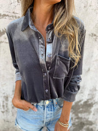 Frau in grauem Samthemd und Jeansshorts vor Betonwand.