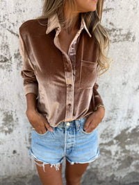 Frau in brauner Samtbluse und blauen Jeansshorts vor Betonwand.