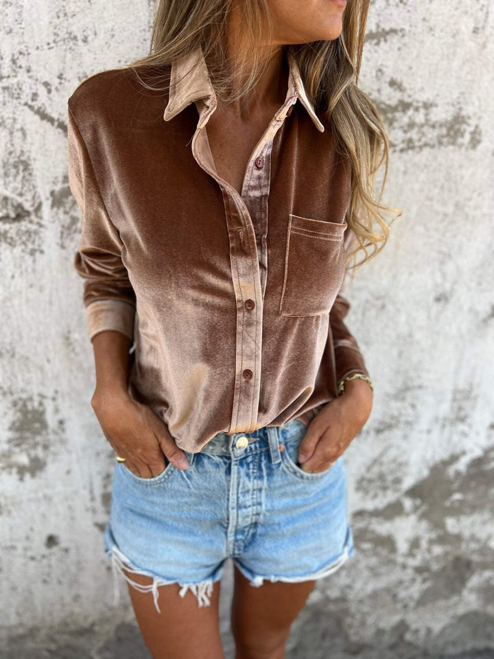 Frau in brauner Samtbluse und blauen Jeansshorts vor Betonwand.