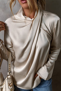 Frau in cremefarbener Satinbluse mit Drapierung, Jeans und beiger Handtasche.