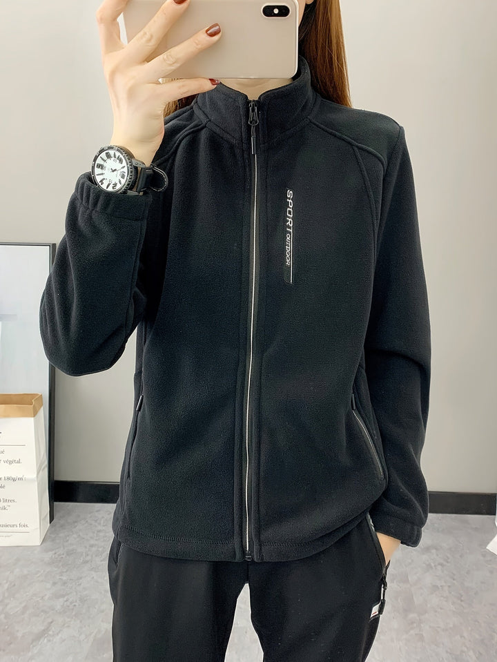 Frau in schwarzer Fleecejacke mit Reißverschluss, Sportuhr, Smartphone, Indoor-Hintergrund.