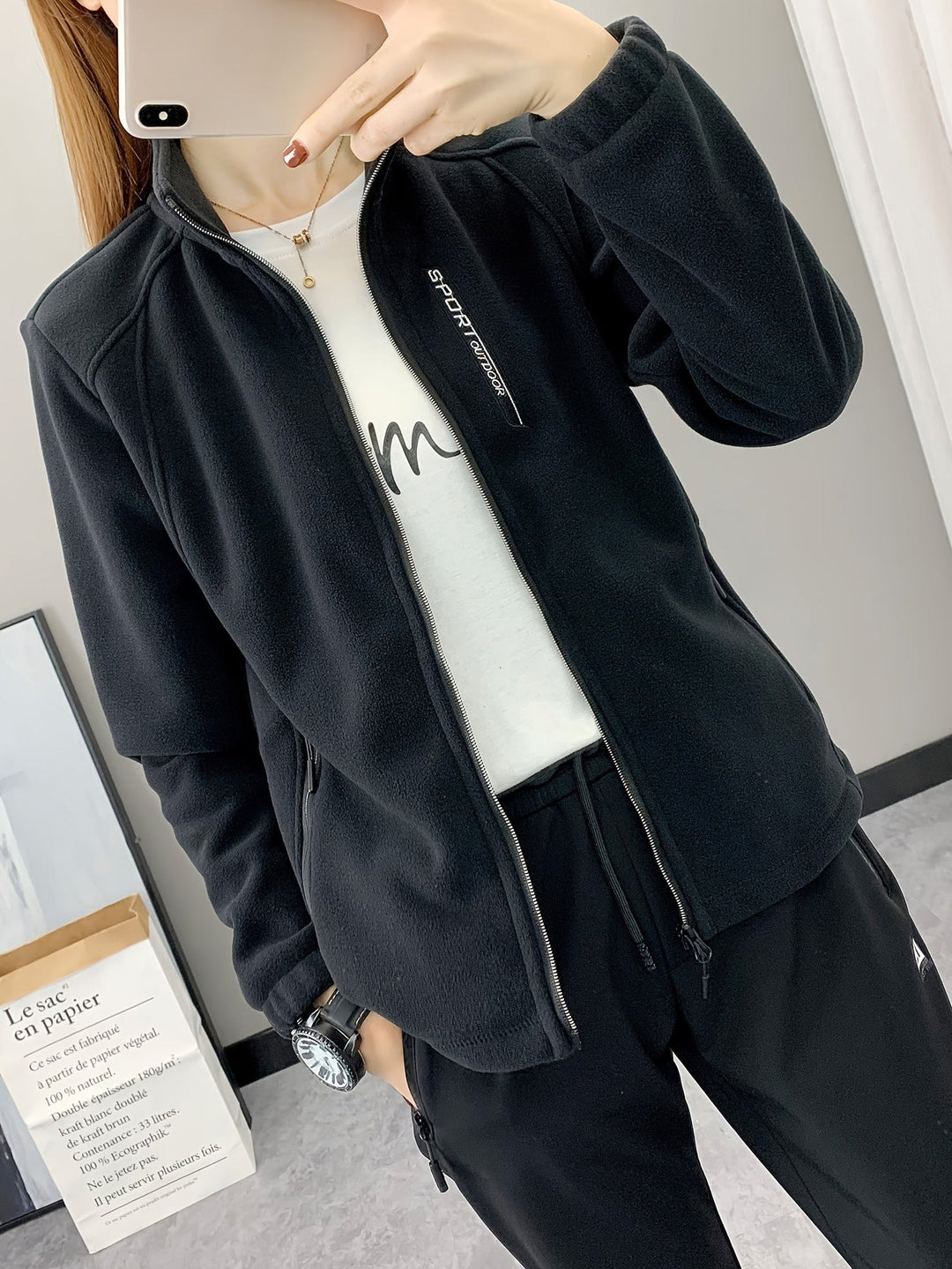 Frau in schwarzer Fleecejacke, Sportbekleidung, Reißverschluss, Indoor, Spiegel-Selfie.