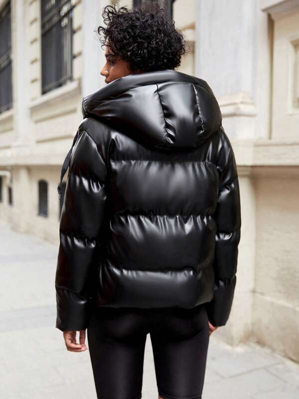 Frau in schwarzer, glänzender Daunenjacke auf städtischer Straße, Wintermode, Outdoor-Bekleidung.