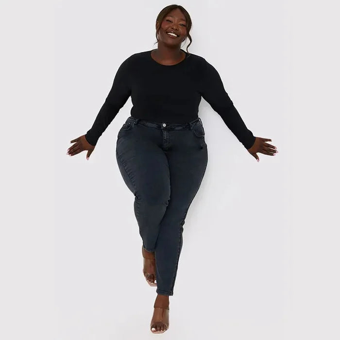 Frau in schwarzem Langarmshirt und dunkler Jeans, lächelnd, Plus-Size-Mode, Studioaufnahme.