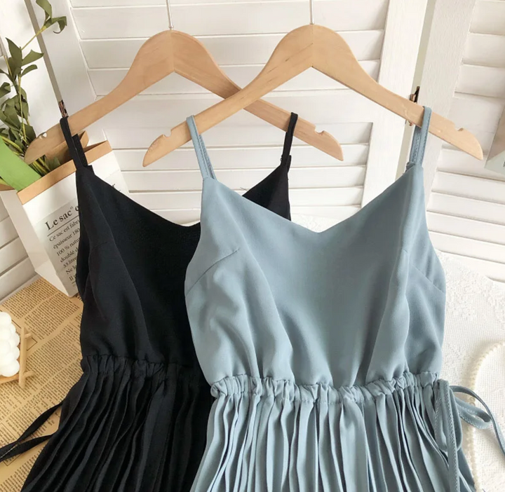 Zwei Sommerkleider auf Holzkleiderbügeln, schwarz und blau, mit Plissee-Details.