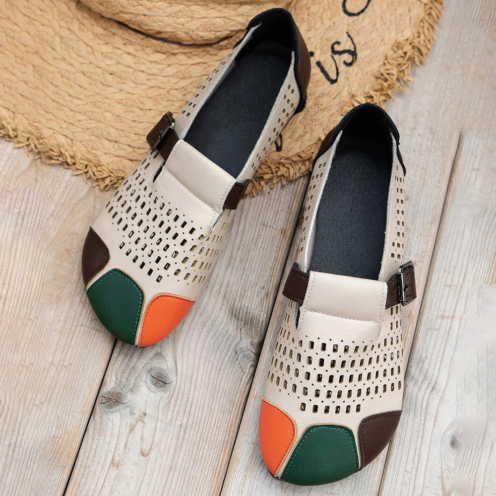 Beige Damen-Loafer mit Lochmuster, farbigen Zehenkappen, aus Leder, auf Holzboden.