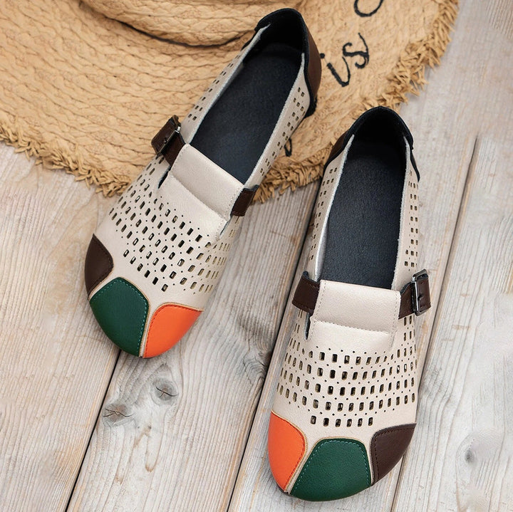 Beige Damen-Loafer mit Lochmuster, farbigen Zehenkappen, aus Leder, auf Holzboden.