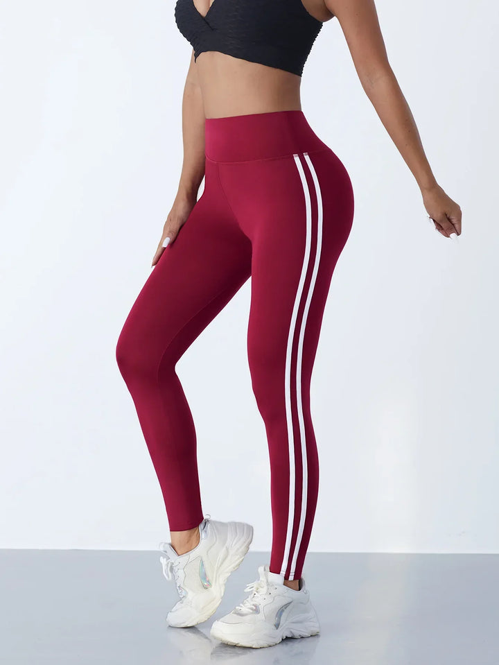 Frau in roten Sportleggings mit weißen Streifen, schwarze Sport-BH, weiße Turnschuhe.
