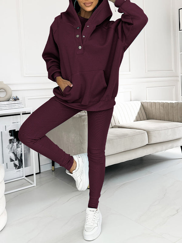 Frau in burgundfarbenem Jogginganzug, Kapuzenpullover und Leggings, weiße Sneaker, modernes Wohnzimmer.