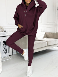 Frau in burgundfarbenem Jogginganzug, Kapuzenpullover und Leggings, weiße Sneaker, modernes Wohnzimmer.