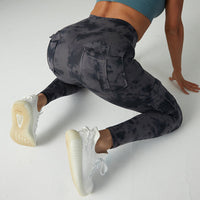 Frau in grauer Camouflage-Leggings beim Sport, weiße Sneaker, Fitnessmode, Rückansicht.