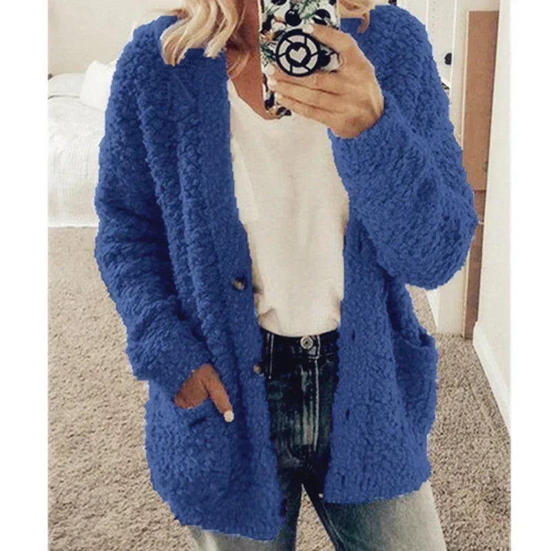 Frau in blauem Strickcardigan, weißem T-Shirt und Jeans, hält Smartphone.