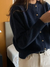 Frau in dunkelblauer Strickjacke mit goldenen Knöpfen, beige Hose, modernes Outfit.