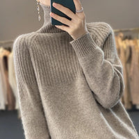 Frau in beigem Strickpullover mit hohem Kragen, hält Smartphone, modisches Herbstoutfit.