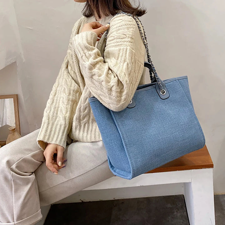 Frau mit blauer Stofftasche, Kettengriff, cremefarbener Strickpullover, modisch, lässig.