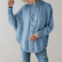 Frau in hellblauem Strickpullover mit Zopfmuster und Jeans, modisch, gemütlich.