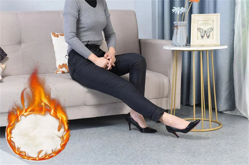Frau in schwarzer Hose und grauem Pullover auf Sofa, trägt schwarze High Heels, Flammensymbol.