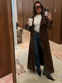 Frau im braunen Trenchcoat, Jeans, Sonnenbrille, hält Kaffeebecher, Selfie im Spiegel.