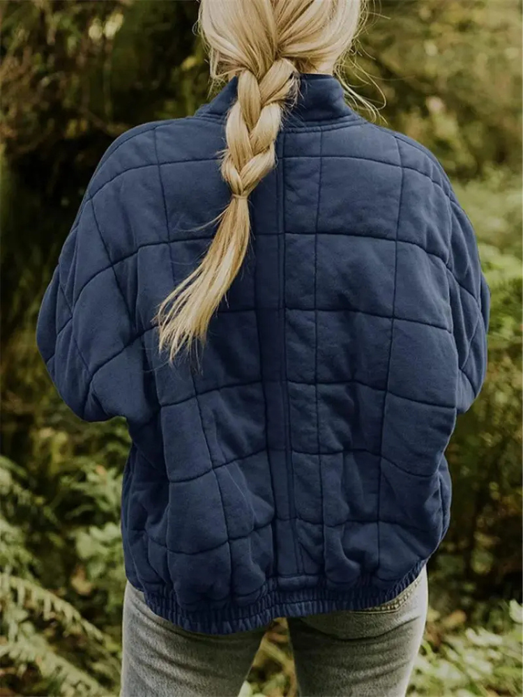 Frau in blauer, gesteppter Übergangsjacke im Wald, blonde Zopf, Herbstmode Damenjacke.