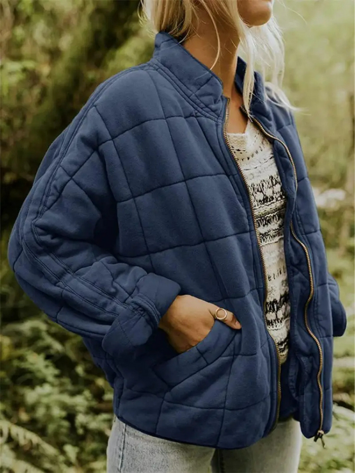 Frau in blauer, gesteppter Übergangsjacke, oversized, mit Reißverschluss, im Freien.