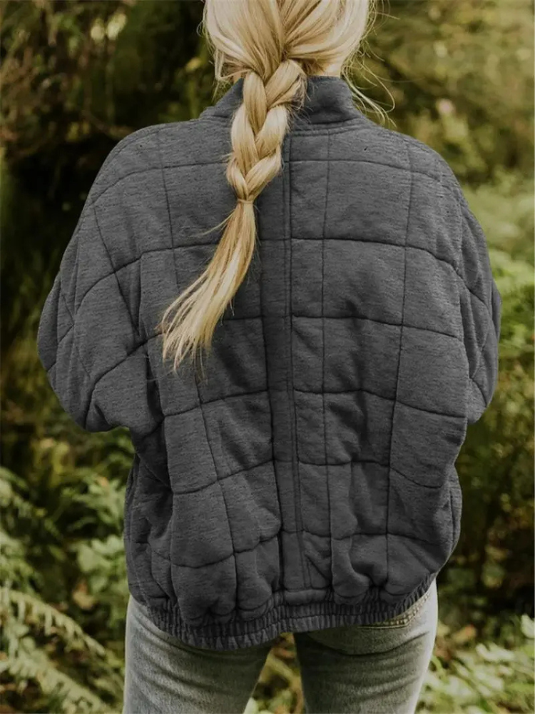 Frau in grauer, gesteppter Übergangsjacke im Wald, oversized Design, Herbstmode.