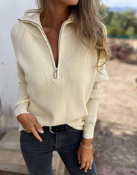 Frau in cremefarbenem Strickpullover mit Reißverschluss, lässiger Herbstmode, draußen.